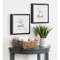 A bathrooms entry stand holding a plant and bin with washcloths in it. It has two frames with posters labeled wash, respectively, with their own designs